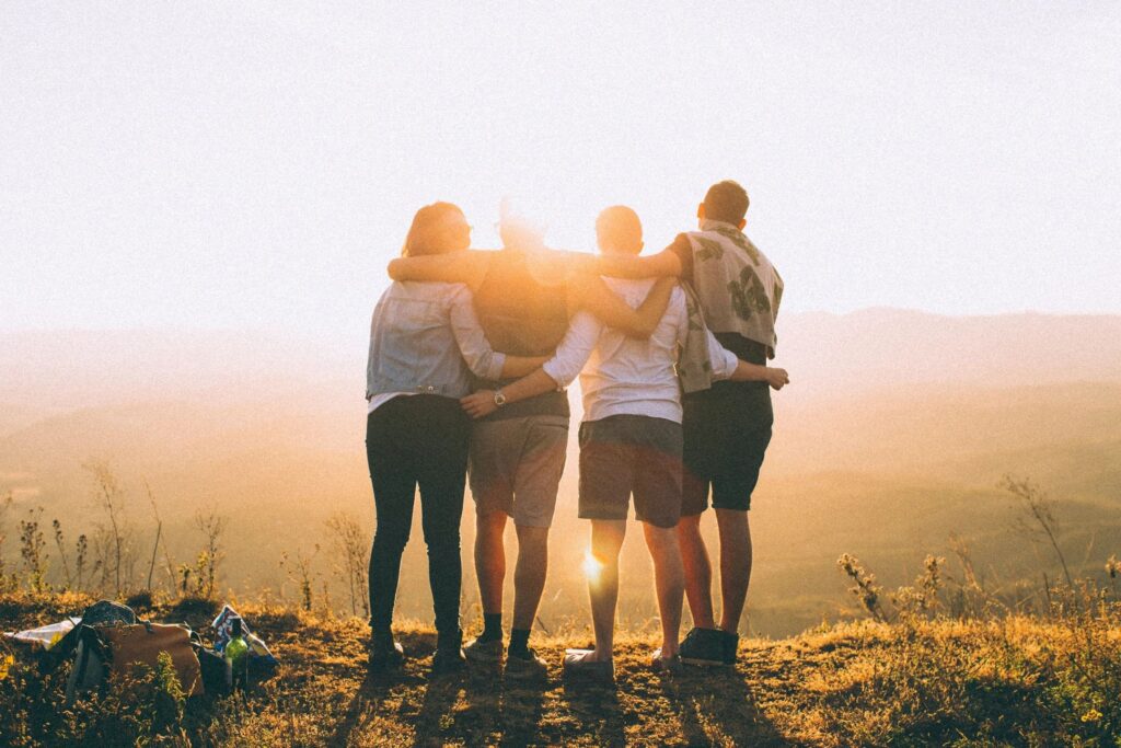 Four individuals, arm-in-arm watching a sunset.
